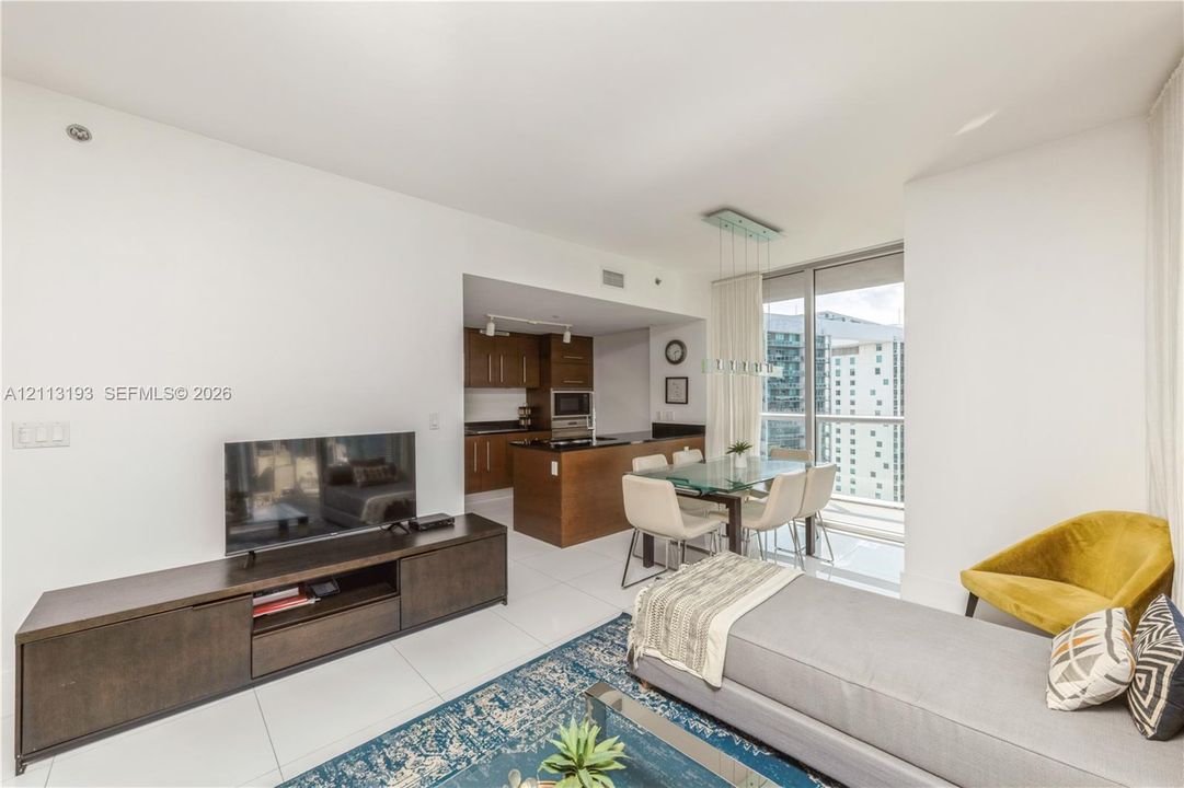 Open-concept living space featuring high-gloss tile flooring, floor-to-ceiling windows, and a kitchen with dark-finish wood cabinetry and a central island