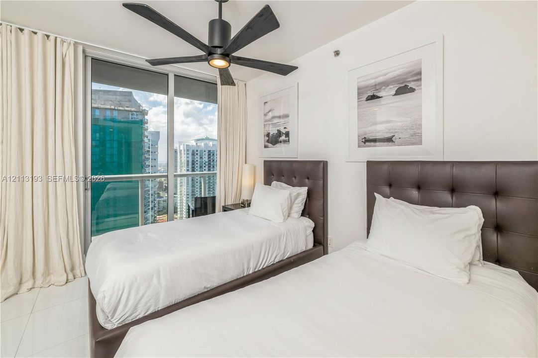 Floor-to-ceiling glass sliding doors with access to a balcony, matte black ceiling fan, and large-format tile flooring