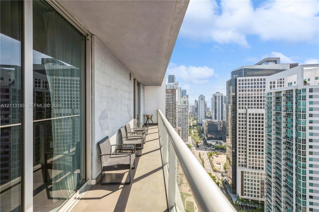 Covered balcony featuring concrete flooring, a glass-panel railing, and floor-to-ceiling sliding glass doors