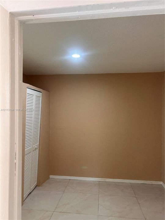 Neutral-toned interior room featuring large-format tile flooring, recessed lighting, and a built-in closet with white louvered doors
