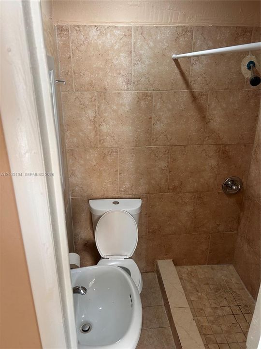 Full-height wall tile, tiled shower surround, integrated shower floor, porcelain toilet, and wall-mounted sink