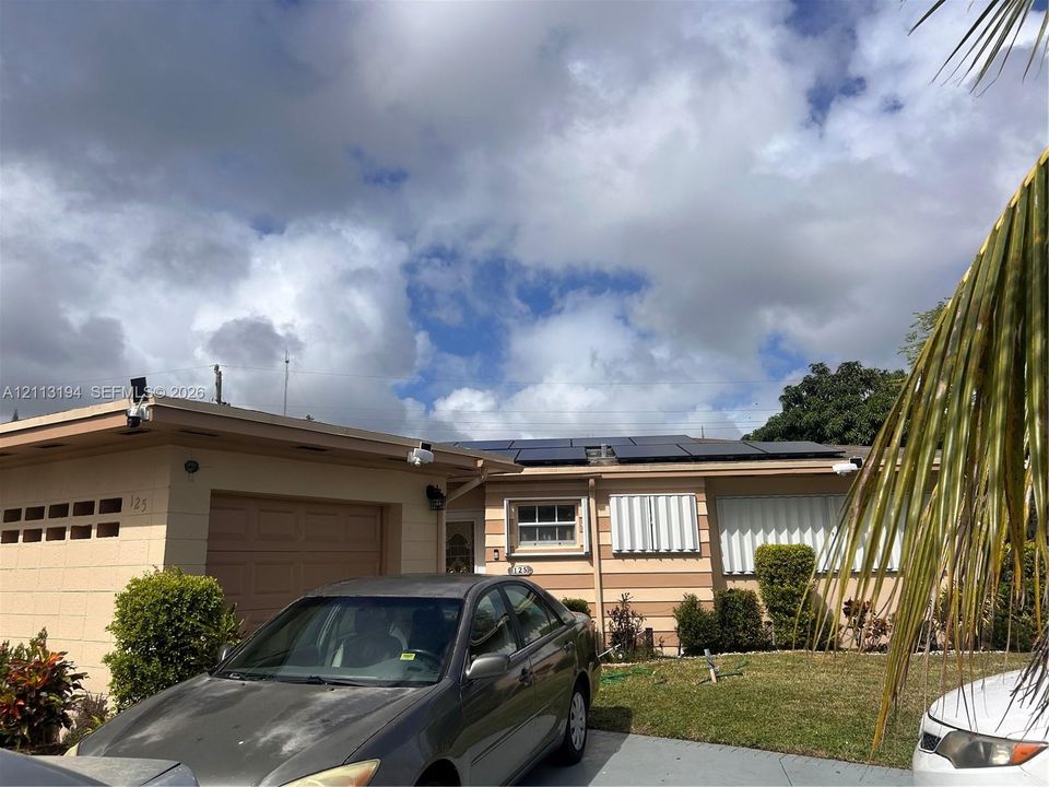 Single-story exterior featuring a concrete block facade, an attached garage, and roof-mounted solar panels