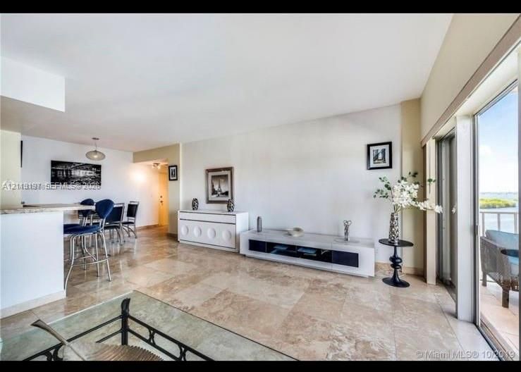 Open-concept interior featuring large-format tile flooring, a breakfast bar with stone-finish countertop, and floor-to-ceiling sliding glass doors