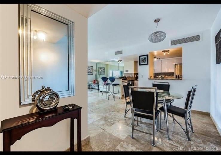 Stone-tile flooring, wall-mounted mirrored panel, textured dome pendant lighting, and pass-through window with granite-style countertop