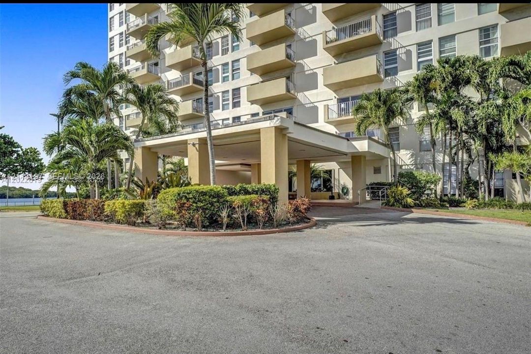 Multi-story residential building exterior featuring a covered porte-cochère, private balconies, and landscaped grounds with mature palm trees