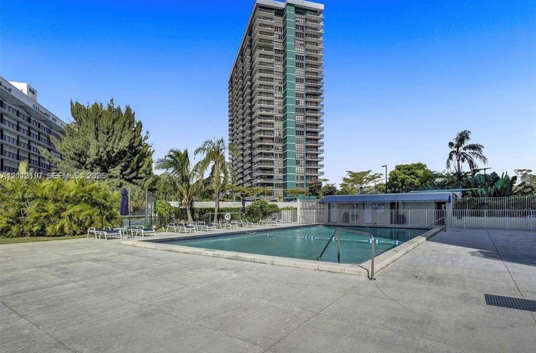 Outdoor swimming pool with concrete decking, surrounding perimeter fencing, and mature landscaping