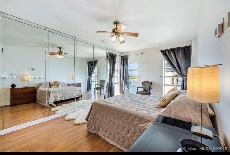 Floor-to-ceiling mirrored wardrobe doors, wood-finish flooring, and a ceiling fan with integrated lighting