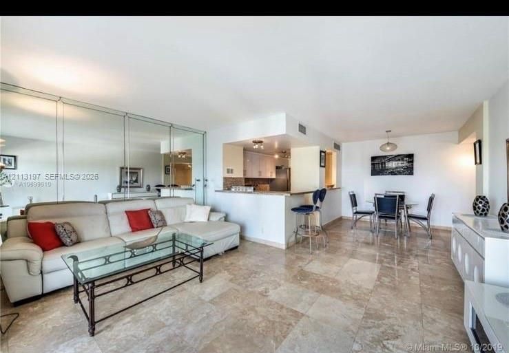 Open-concept space featuring polished stone flooring, a mirrored wall accent, and a breakfast bar