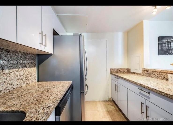 Kitchen featuring high-gloss white cabinetry, stone-finish countertops, stainless steel refrigerator, and integrated dishwasher