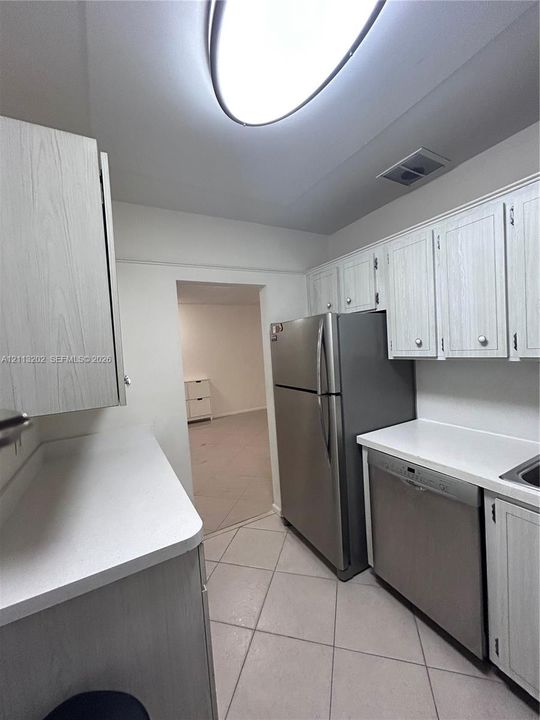 Kitchen featuring wood-grain cabinetry, solid surface countertops, stainless steel refrigerator, stainless steel dishwasher, and tile flooring