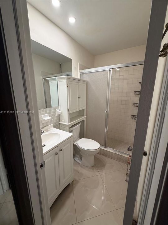 Bathroom featuring tile flooring, a white vanity cabinet with an integrated sink, a built-in storage hutch, and a glass-enclosed shower with tiled walls