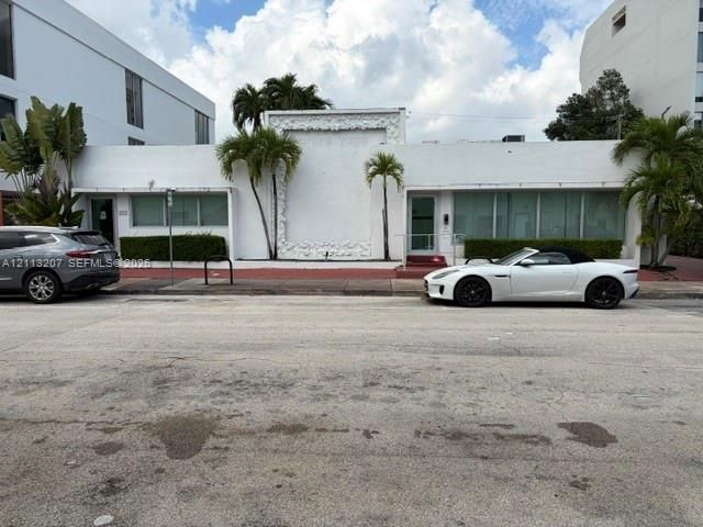 Low-rise commercial facade featuring a textured decorative central panel, white stucco exterior, expansive glass-paneled windows, and integrated landscaping with mature palms