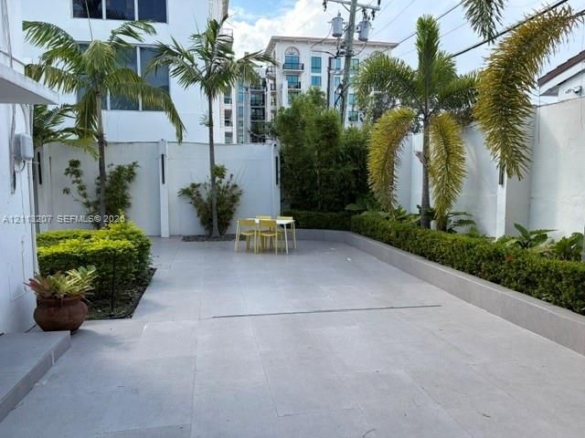 Enclosed courtyard featuring large-format tile flooring, perimeter privacy walls, integrated garden beds, and mature palm trees