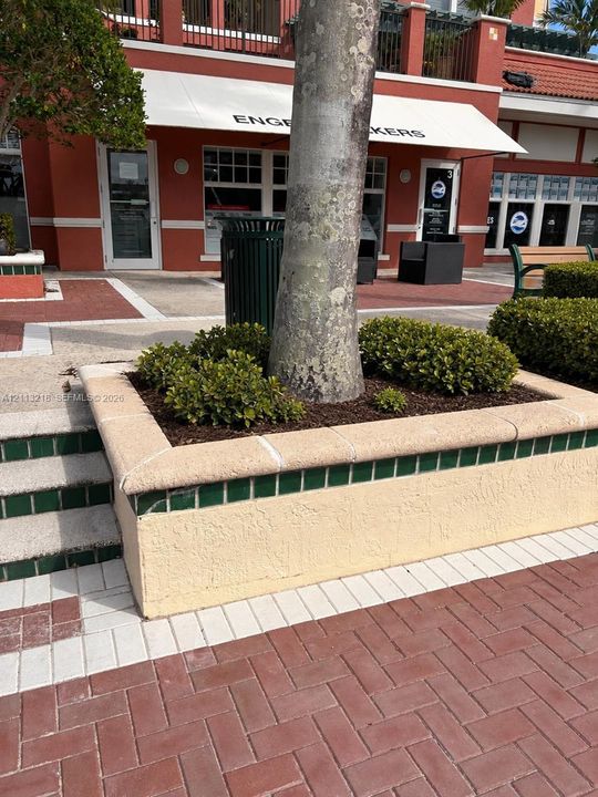 Stucco planter with green tile accents and stone cap, herringbone-patterned brick paver walkway, and built-in masonry steps