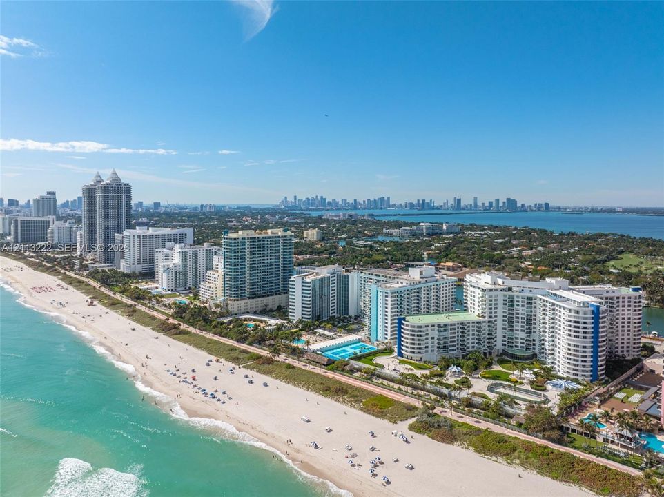Aerial perspective featuring oceanfront location with immediate sandy beach access and proximity to regional metropolitan skyline