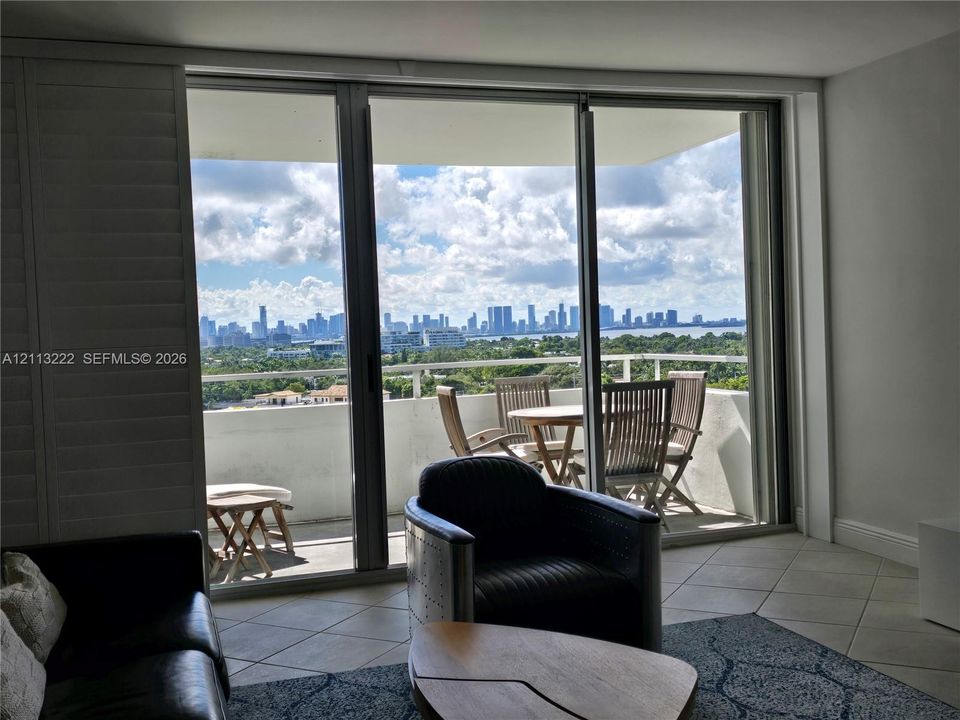 Floor-to-ceiling glass sliding doors opening to an expansive balcony with metal railings and a panoramic skyline backdrop