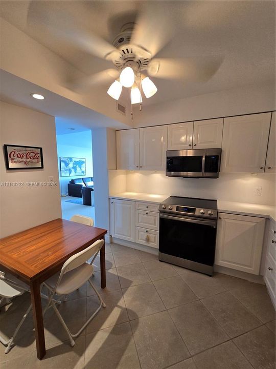 Kitchen featuring white cabinetry, stainless steel microwave and oven, under-cabinet lighting, and tile flooring