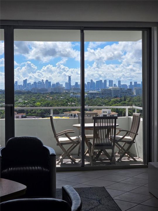 Floor-to-ceiling sliding glass door opening to a private balcony with a metal railing and panoramic city skyline backdrop
