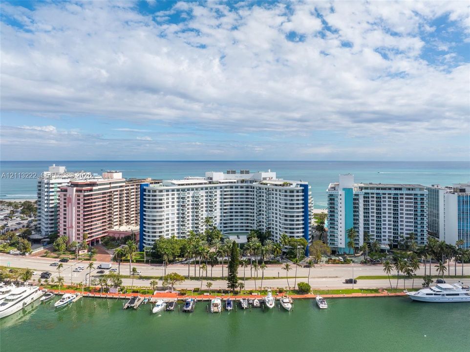 Multi-story high-rise building with a curved façade and multiple balconies, situated on a waterfront lot with an anchored private dock