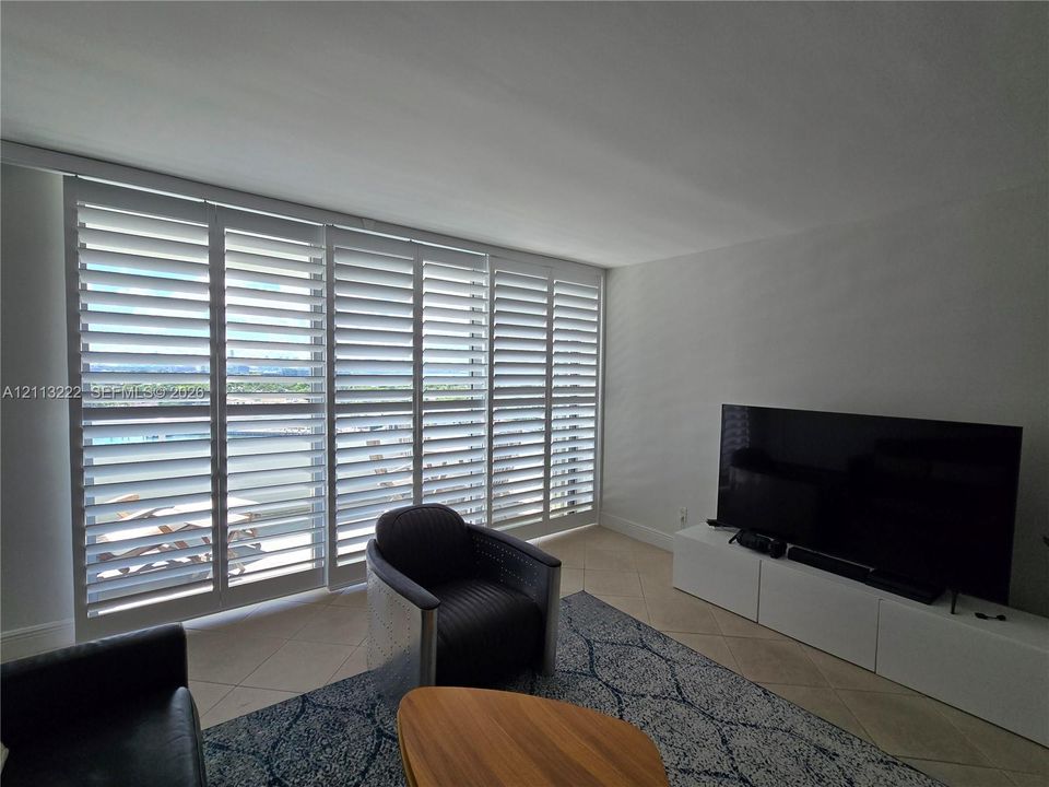 Floor-to-ceiling sliding glass doors featuring white plantation shutters and light-toned tile flooring