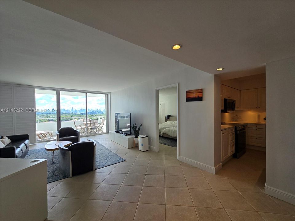 Open living area featuring large-format ceramic tile flooring, recessed lighting, expansive glass sliding doors, and a kitchen with white cabinetry
