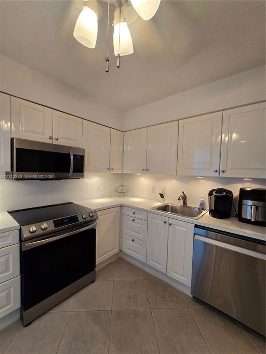Kitchen featuring white high-gloss cabinetry, stainless steel appliances, solid surface countertops, tile flooring, and under-cabinet lighting