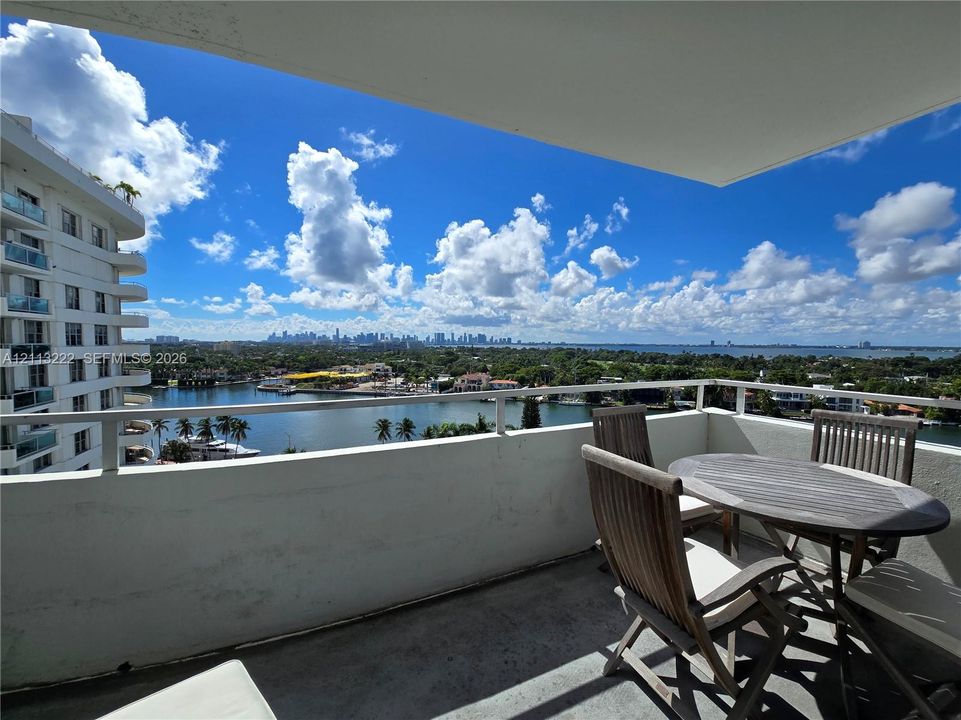 Covered balcony featuring concrete flooring and a metal railing, overlooking a waterway and the distant skyline