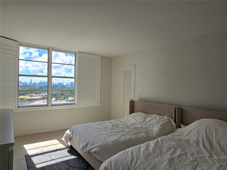 Room featuring expansive windows, louvered interior shutters, large-format tile flooring, and a closet with a louvered door