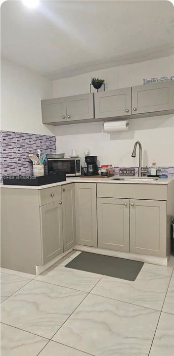 Kitchenette featuring light-toned shaker-style cabinetry, a stone-composite countertop, a high-arc faucet with an undermount sink, a mosaic-tiled backsplash, and large-format porcelain tile flooring