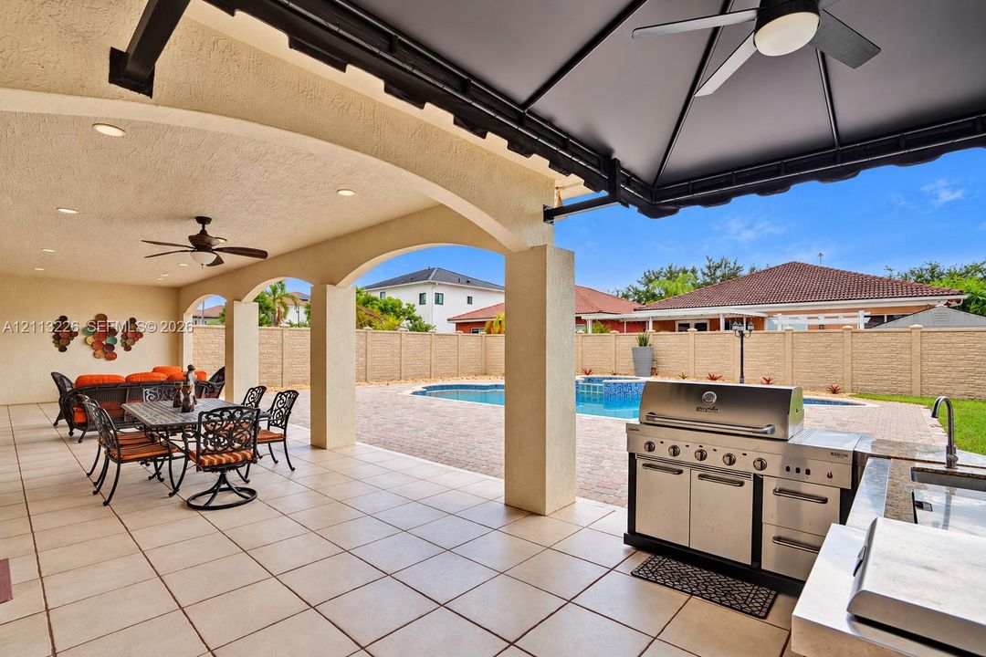 Covered lanai featuring arched stucco columns, recessed lighting, ceiling fans, built-in stainless steel outdoor kitchen, and concrete patio tiling