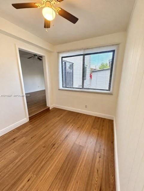 Interior space featuring wood-finish flooring, a ceiling fan with integrated light fixture, and a large window with horizontal blinds
