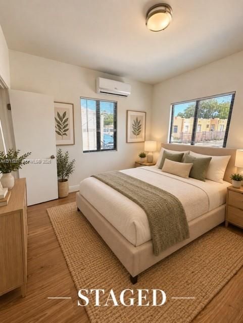 Wood-finish flooring, dual windows with black-framed trim, wall-mounted ductless climate control unit, and a central flush-mount ceiling light fixture