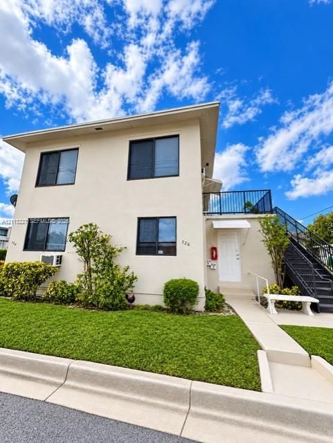 Two-story exterior featuring a smooth stucco facade, metal-railed staircase, elevated balcony, and paved walkway