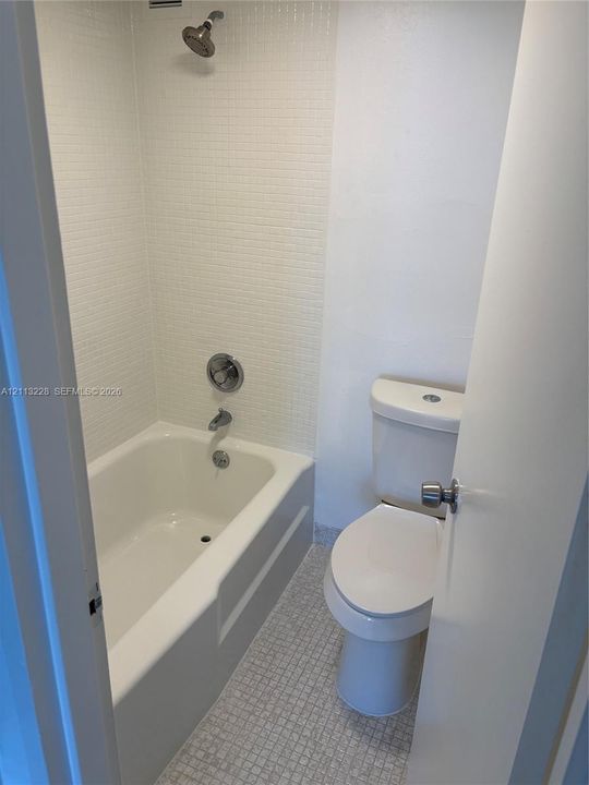 Bathtub with a showerhead, white wall-mounted mosaic tile surround, and a standard-height toilet