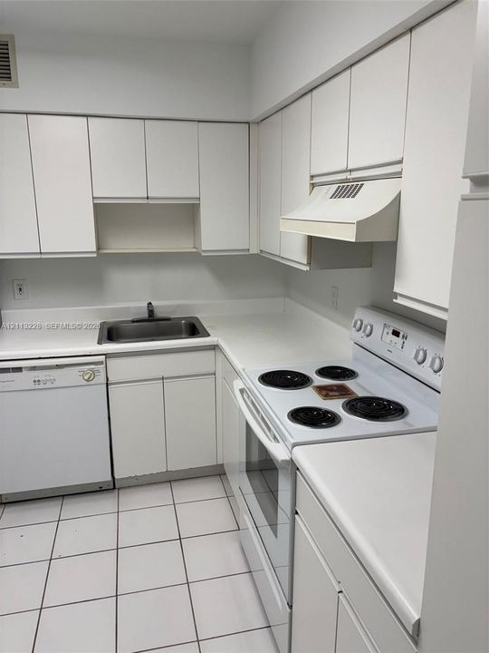 Kitchen featuring white cabinetry, solid-surface countertops, integrated range hood, built-in dishwasher, and ceramic tile flooring
