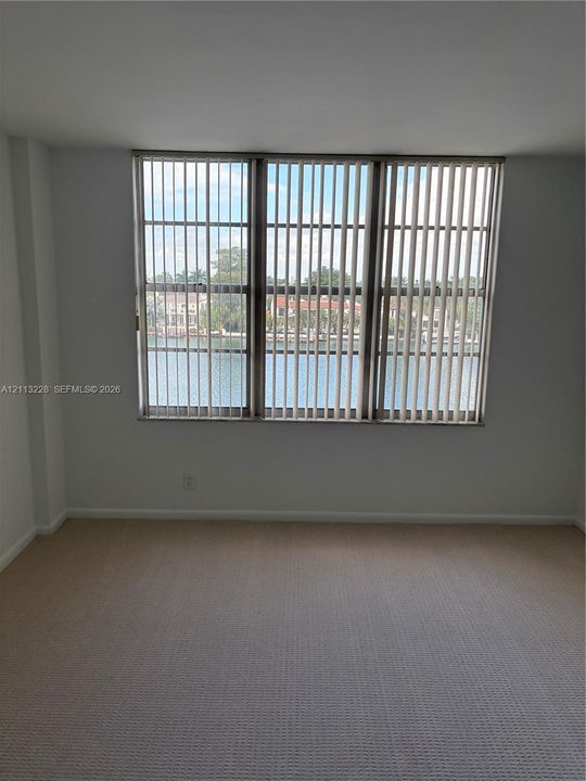 Wall-to-wall carpeting and a triple-pane window featuring vertical blinds with a water-facing exposure