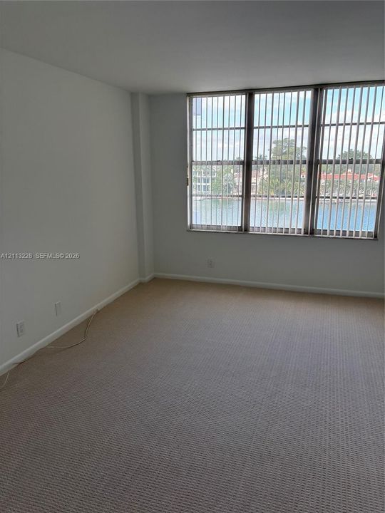 Neutral-toned carpeting, expansive window wall with water scenery, and vertical blinds