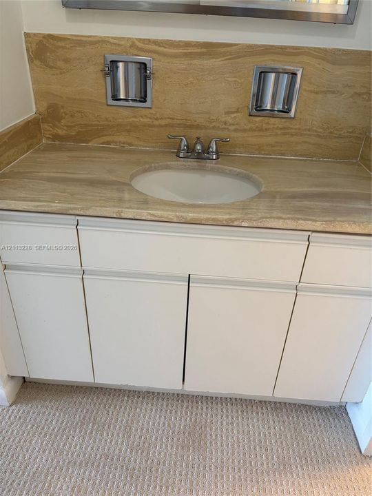 Vanity with off-white cabinetry, stone-finish countertop and matching backsplash, integrated oval sink, and metallic dual-handle faucet