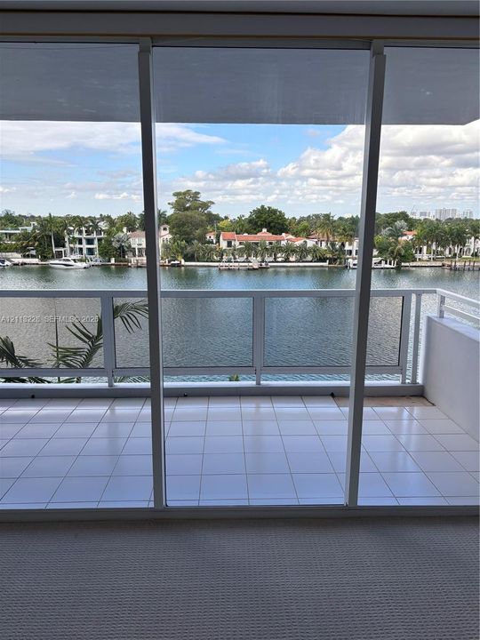 Covered balcony with white tile flooring and a glass-panel railing overlooking the water