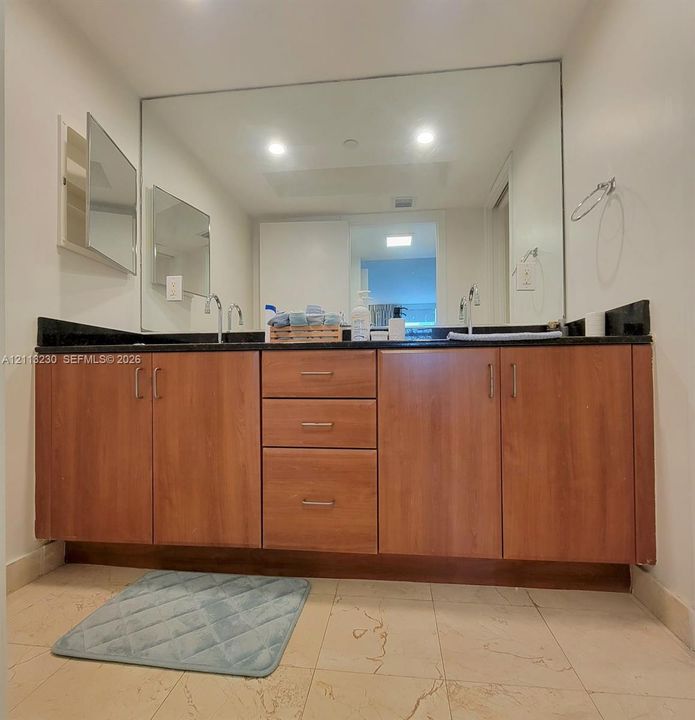 Dual-sink vanity featuring wood-finish cabinetry, dark solid-surface countertops, recessed medicine cabinet, and a full-width wall mirror