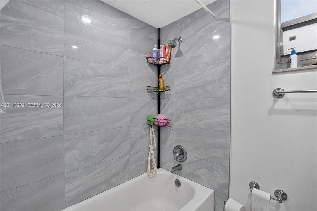 Bathtub surround featuring large-format gray veined tile, integrated metallic shower head, and wall-mounted metal towel rack