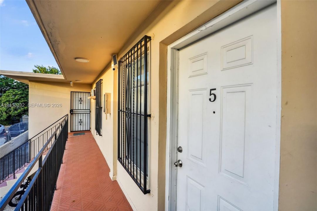 Exterior walkway with tiled flooring, metal railings, and unit entry door featuring protective iron security bars on window openings