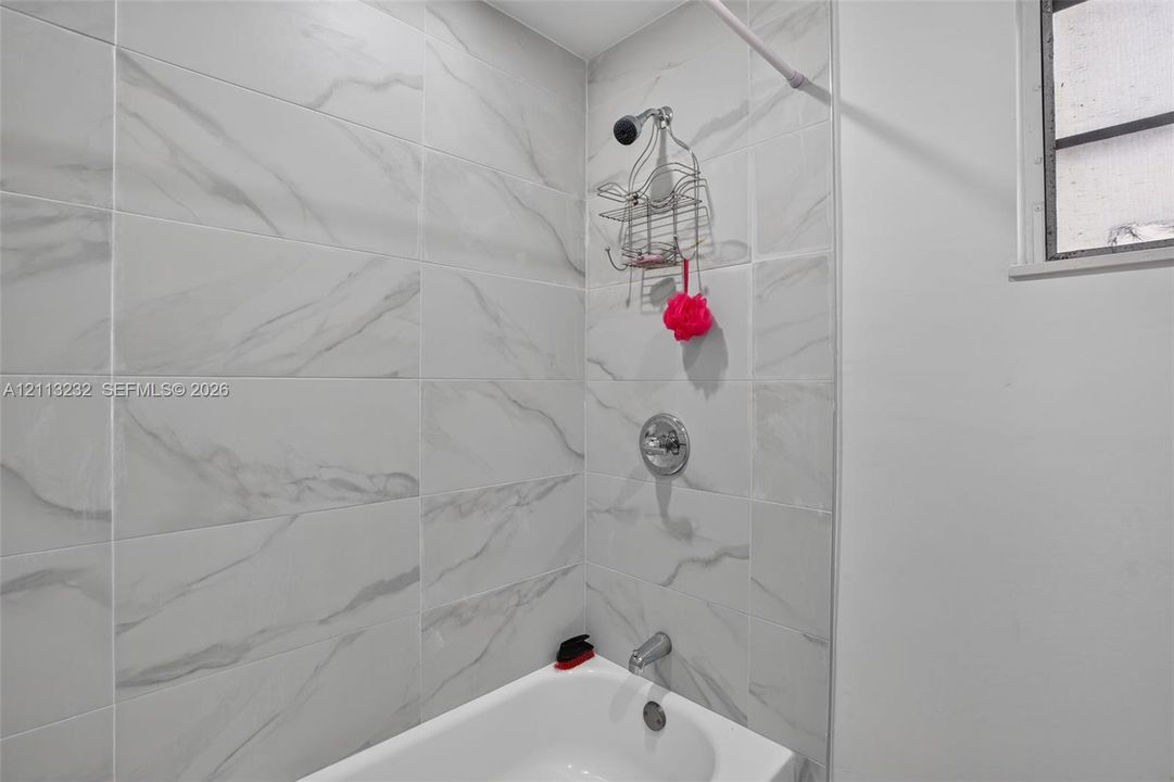 Full-height shower enclosure featuring large-format stone-patterned wall tile, chrome plumbing fixtures, and a white soaking tub