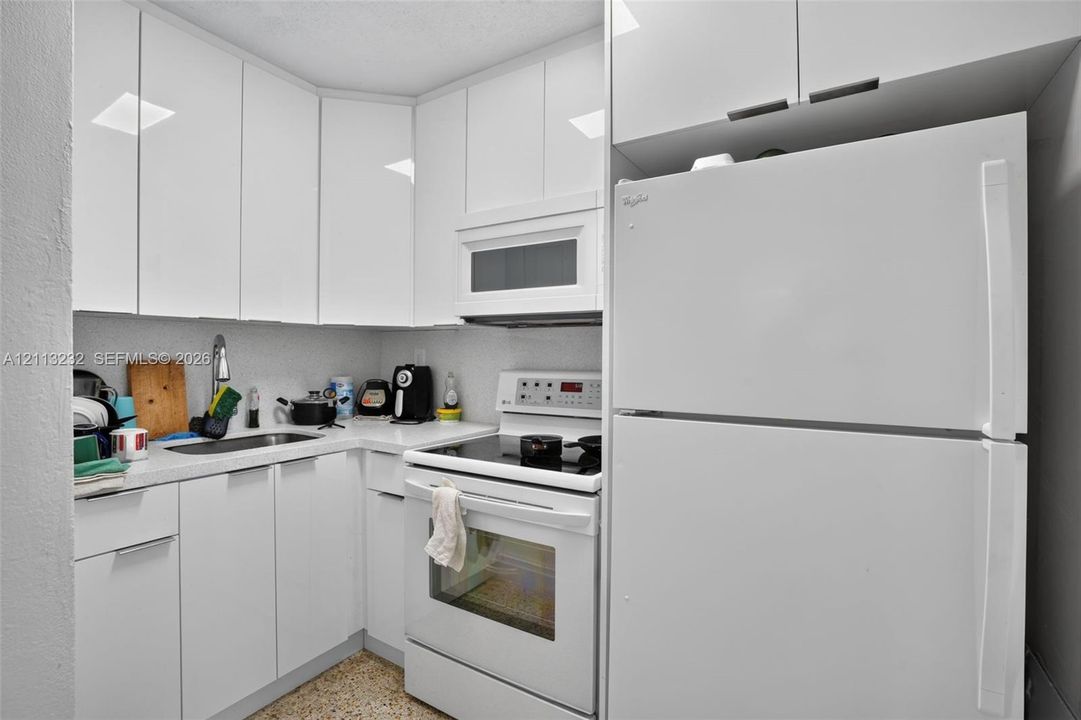 Kitchen featuring high-gloss white cabinetry, solid-surface countertops, stainless steel sink with high-arc faucet, and white appliances including a built-in microwave and range