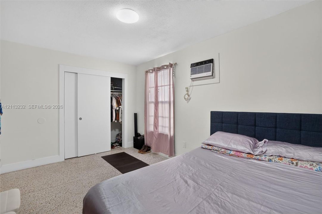 Room featuring sliding-panel closet doors, wall-mounted air conditioning unit, neutral wall finishes, and overhead flush-mount lighting