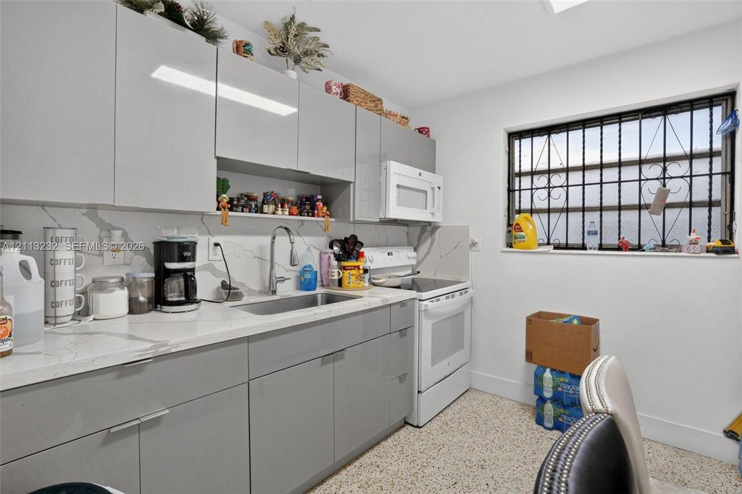 Kitchen featuring high-gloss gray cabinetry, stone-patterned countertops, a full-height stone-patterned backsplash, undermount stainless steel sink with a high-arch faucet, and terrazzo flooring