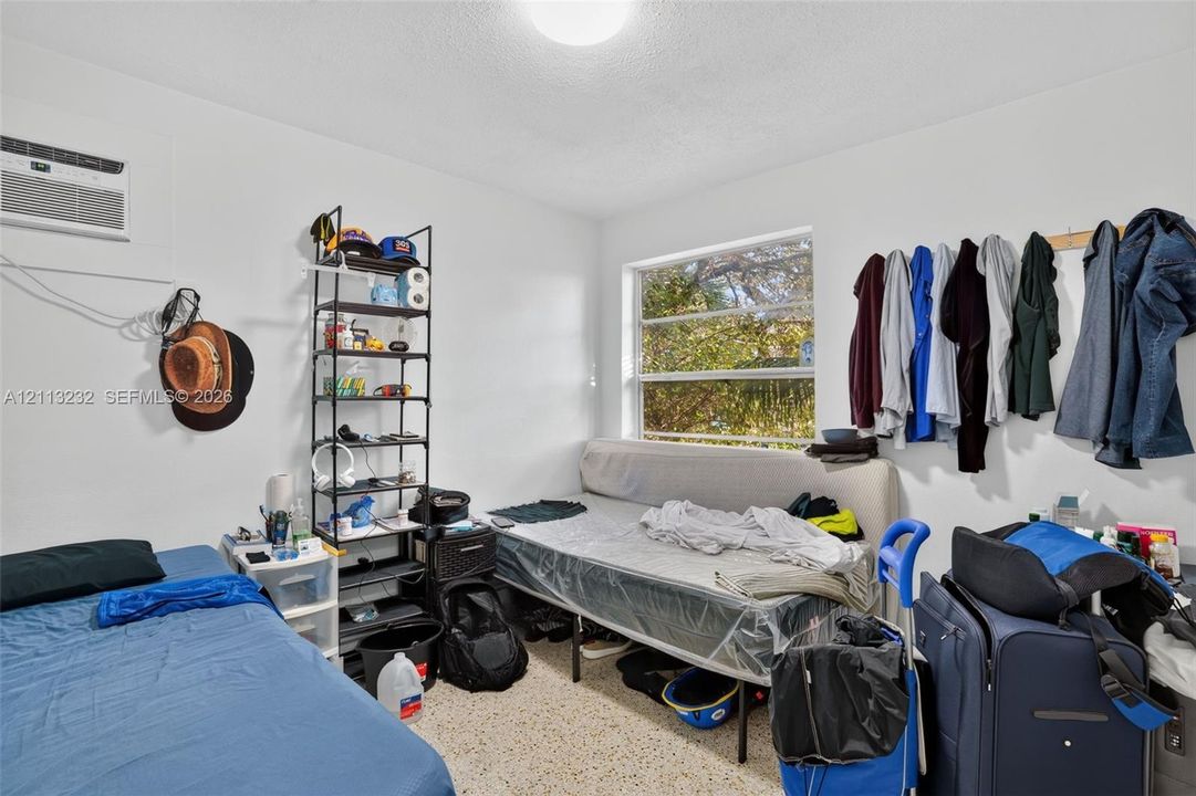 Room featuring white walls, terrazzo flooring, a window, and a wall-mounted air conditioning unit