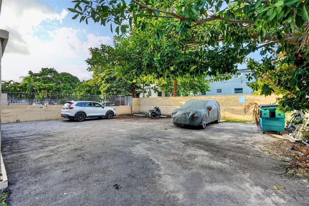 Asphalt parking area enclosed by a perimeter masonry wall and chain-link fencing, complemented by mature shade trees