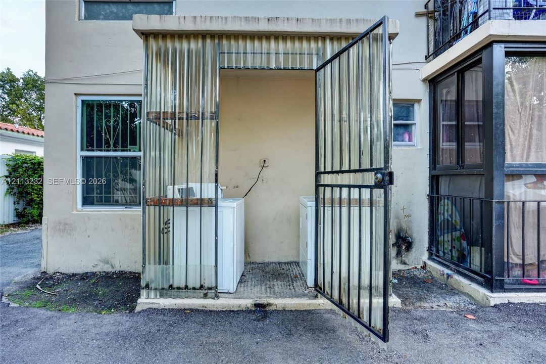Exterior laundry area enclosed by corrugated polycarbonate panels and a metal security gate
