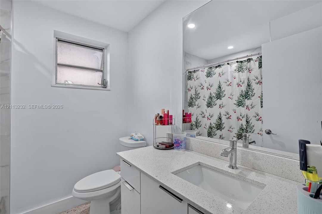 Bathroom featuring a vanity with a light-toned speckled countertop, an undermount rectangular sink, a chrome faucet, and a large-format vanity mirror with recessed lighting